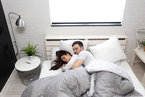 Νεαρό ζευγάρι στον ύπνο σε κρεβάτι στην κρεβατοκάμαρα - Φωτογραφία, εικόνα