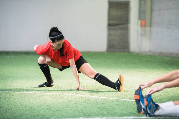 Aktivní dívka ve sportovní uniformě dělá cvičení pro protahování nohou na fotbalovém hřišti při tréninku před zápasem - Fotografie, Obrázek
