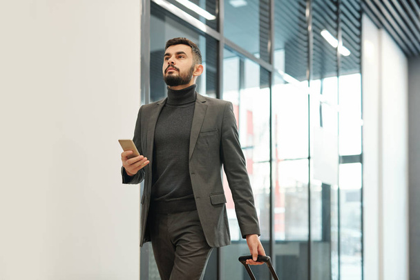 Giovane uomo d'affari in formalwear tirando valigia mentre si muove verso l'uscita attraverso l'aeroporto durante il viaggio
 - Foto, immagini