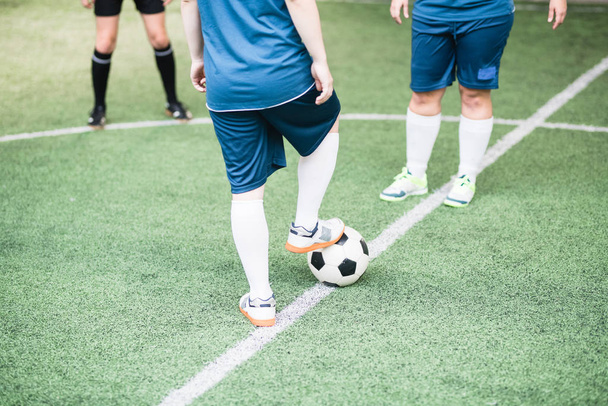 フィールド上の他の女の子の前に立っている間若い女性サッカー選手はサッカーボールの上に右足を維持 - 写真・画像