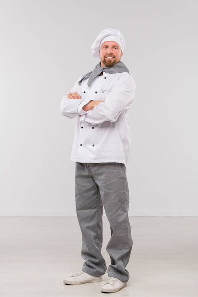 Succesvolle jonge mannelijke chef-kok met zijn armen gekruist door borst te kijken naar je terwijl hij in isolatie staat - Foto, afbeelding
