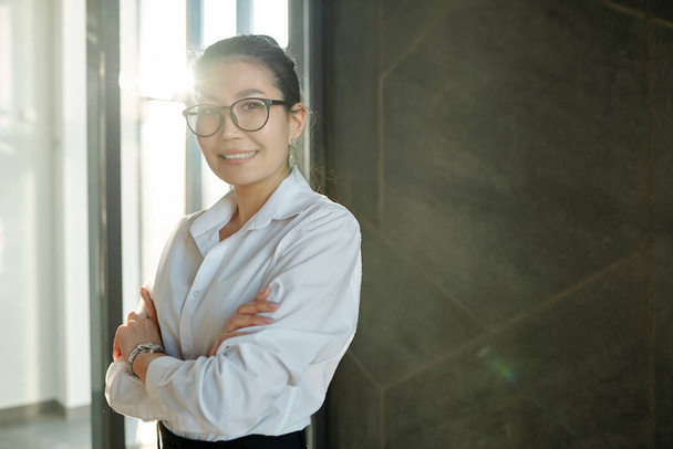 Bonita jovem sorridente empresária de etnia asiática com braços cruzados olhando para você dentro do aeroporto
 - Foto, Imagem
