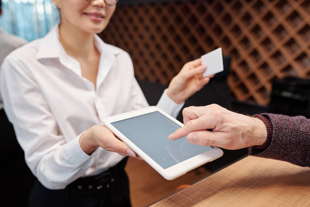Egy érett üzletember keze, aki táblagépre mutat, hogy aláírja, mielőtt kiveszi a kártyát a hotelszobából. - Fotó, kép