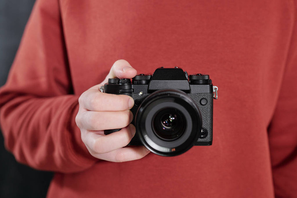 Руки современного фотографа-мужчины в коричневой толстовке с новой фотокамерой перед собой
 - Фото, изображение