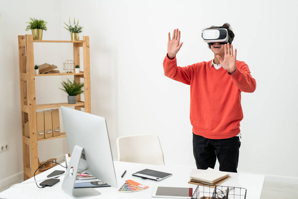Opgewonden freelancer in casualwear en vr headset aanraken van virtuele display tijdens het ervaren van een andere realiteit - Foto, afbeelding