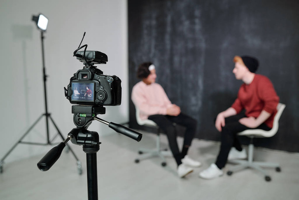 Pantalla de videocámara digital con dos vloggers sentados en sillas uno frente al otro y hablando en estudio
 - Foto, imagen