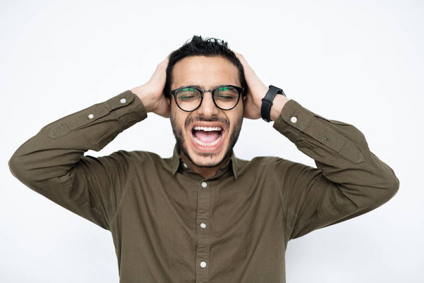 irritierter junger Geschäftsmann gemischter Rassen mit Brille hält seine Hände auf dem Kopf, während er in Isolation schreit - Foto, Bild