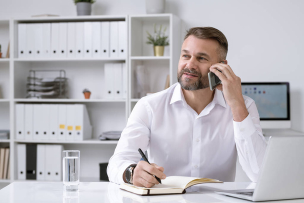 Bearded confident director of business company phoning client or partner while solving organization questions in office - Фото, изображение