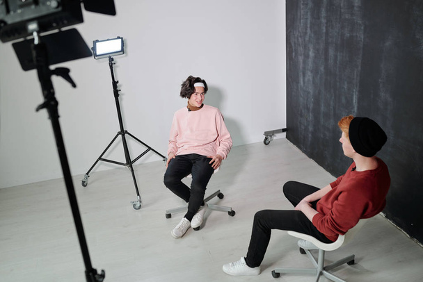 zwei freundliche Vlogger in schwarzen Jeans und Sweatshirts diskutieren zeitgenössische Informationsquellen, während sie sich im Studio versammeln - Foto, Bild