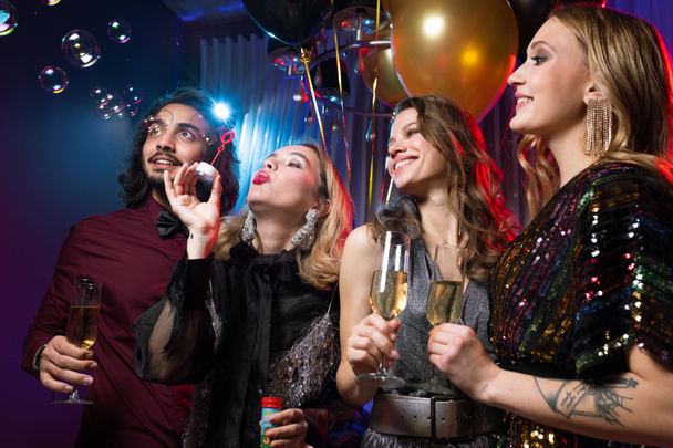 Glamouröses Mädchen pustet bei Geburtstagsparty Seifenblasen unter Freunden mit Champagner-Flöten - Foto, Bild