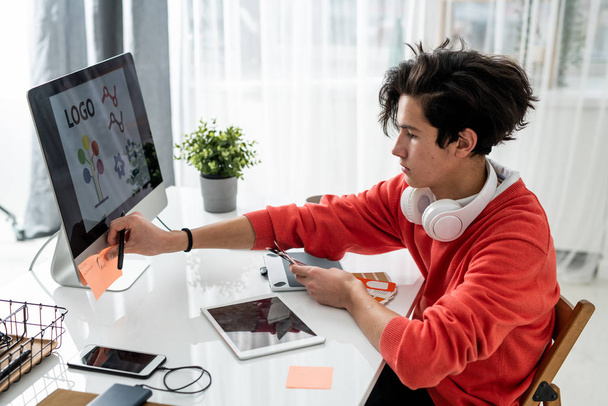 Giovane designer maschio con campioni di colore che mette appiccicosi appunti sul pannello dello schermo del computer mentre lavora sulla scrivania
 - Foto, immagini