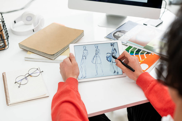 Manos de diseñador de moda creativa con pluma apuntando a la pantalla de la tableta al elegir nuevos modelos para la colección de temporada
 - Foto, imagen