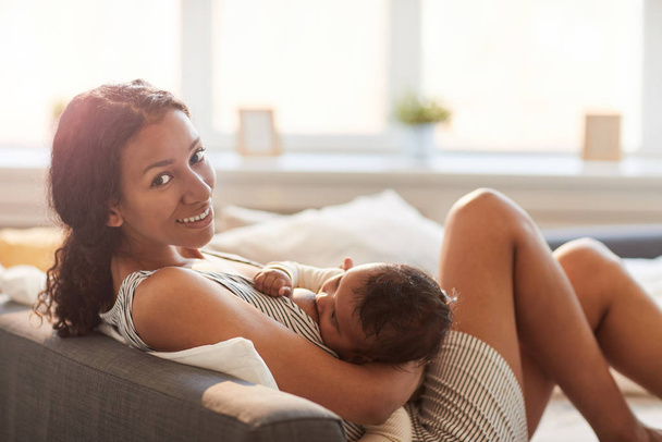 Side view portrait of young African-American mother breastfeeding cute baby boy and looking at camera, copy space - 写真・画像