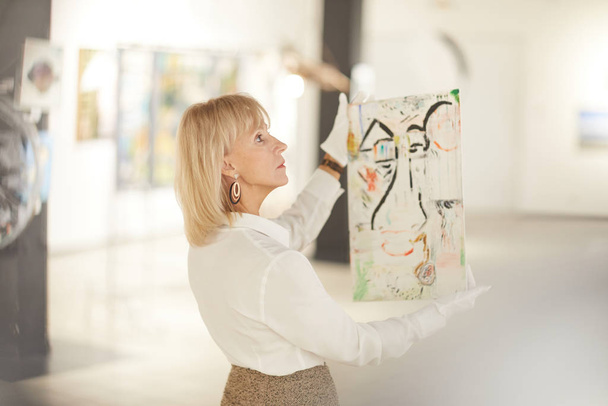 Retrato de especialista em arte feminina segurando pintura enquanto aprecia obras em galeria moderna ou museu, espaço de cópia
 - Foto, Imagem