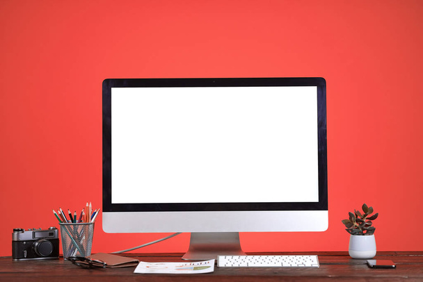 Workplace concept with blank white computer screen at wooden desk over coral background, copy space - Foto, imagen