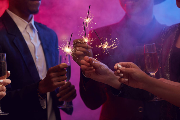 Closeup of young people lighting sparklers while enjoying Christmas party in smoky night club, copy space - Photo, Image
