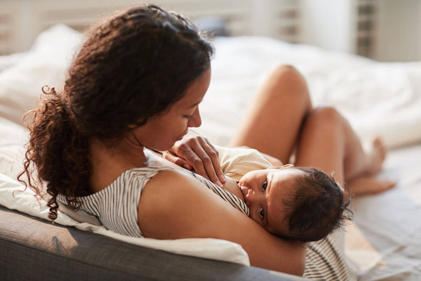 Alto ángulo retrato de la madre afroamericana joven amamantando lindo bebé con niño mirando a la cámara, espacio de copia
 - Foto, Imagen