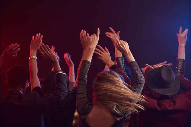 Вид сзади молодых людей, прыгающих и поднимающих руки, наслаждаясь вечеринкой в дымчатом ночном клубе, копирующее пространство
 - Фото, изображение