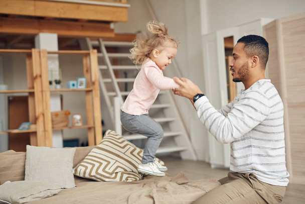 Sivukuva muotokuva söpö pieni tyttö hyppää sohvalla pelatessaan isän kanssa kotona, kopioi tilaa
 - Valokuva, kuva