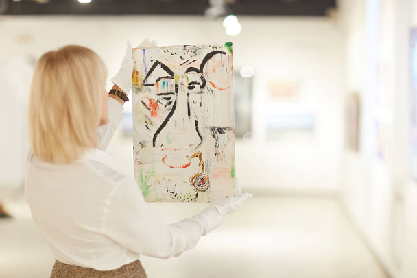 Vista posterior retrato de la mujer experta en arte sosteniendo la pintura, mientras que la valoración de las obras en la galería moderna o museo, espacio de copia
 - Foto, imagen