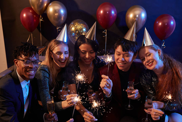 multiethnische Gruppe eleganter junger Leute zündet Wunderkerzen an, während sie Weihnachten während einer Party in einem Nachtclub feiern, Kopierraum - Foto, Bild