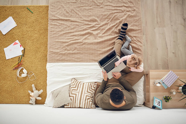 Top view background of little girl playing with father using laptop in cozy bedroom interior, copy space - Photo, Image