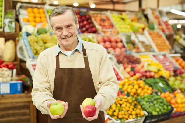 Portrait taille haute d'un homme âgé souriant tenant des pommes fraîches tout en vendant des fruits et légumes au marché fermier, espace de copie
 - Photo, image