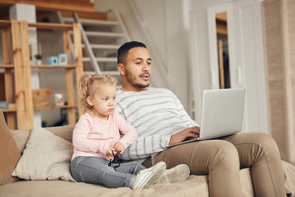 Portrait de mignonne petite fille assise sur un canapé et regardant des vidéos avec papa à l'aide d'un ordinateur portable, espace de copie
 - Photo, image