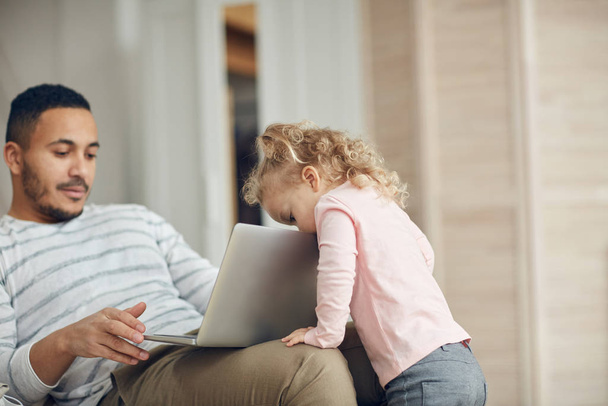 Portré aranyos kislány kukucskál laptop képernyőn, miközben nézi apa dolgozik otthonról, másolás tér - Fotó, kép
