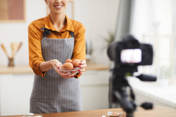 Stüdyoda yemek pişirirken kameraya yumurta tutan güzel bir genç kadın portresi. - Fotoğraf, Görsel