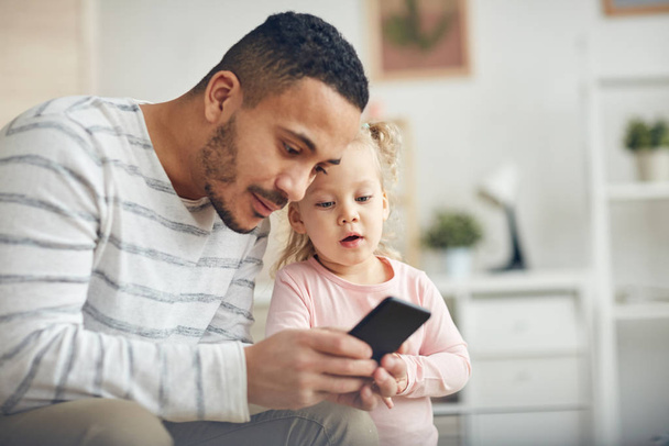 Portret współczesnego taty pokazujący smartfon słodkiej córeczce w domu, przestrzeń do kopiowania - Zdjęcie, obraz