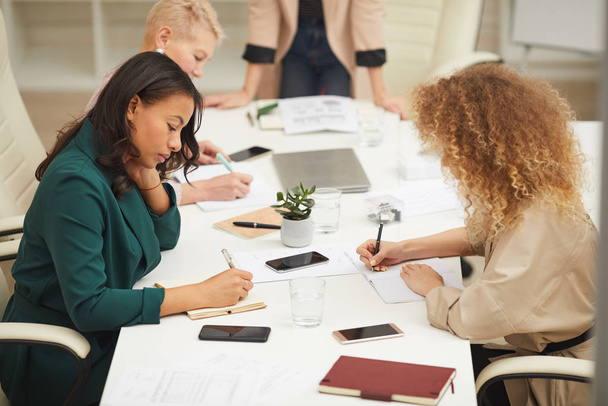 Group of creative businesswomen brainstorming at meeting writing down their ideas in notebooks, horizontal high angle shot - Φωτογραφία, εικόνα
