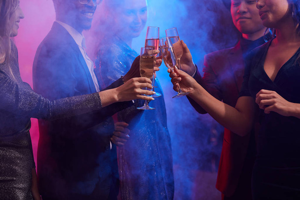 Imagen recortada de los jóvenes tintineando copas de champán en el club nocturno ahumado mientras celebran las vacaciones en la fiesta, espacio para copiar
 - Foto, Imagen