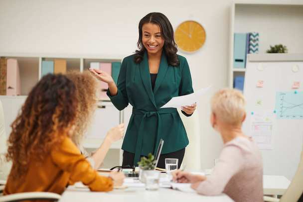 Vrolijke Afro-Amerikaanse zakenvrouwen staan voor haar collega 's praten over nieuwe strategie resultaten horizontaal oog schot - Foto, afbeelding