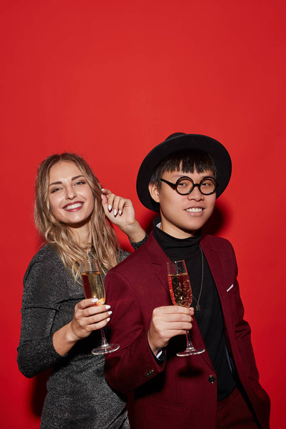 Taille hoch Portrait trendiger junger Leute mit Champagnergläsern beim Feiern, aufgenommen mit Blitz auf rotem Hintergrund - Foto, Bild