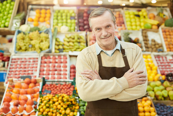 Waist up portrait of smiling senior man looking at camera while selling fruits and vegetables at farmers market, copy space - Photo, Image