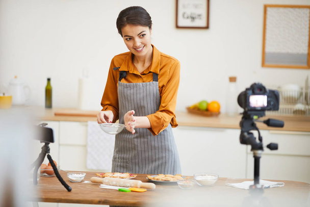 Waist up portrait of beautiful young woman looking at camera while filming baking tutorial for video channel, copy space - Photo, Image
