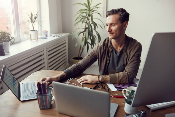 Portret van een knappe, volwassen zakenman die computers gebruikt tijdens multitasking op kantoor, kopieerruimte - Foto, afbeelding