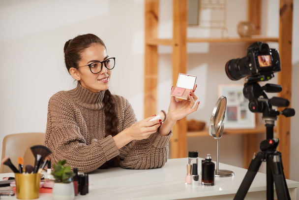 Portret van lachende jonge vrouw tonen make-up producten aan de camera tijdens het filmen video review voor schoonheid en lifestyle kanaal, kopieer ruimte - Foto, afbeelding