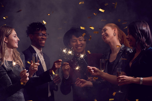Multi-ethnic group of elegant people enjoying Christmas party in smoky night club with glitter falling overhead, copy space - Photo, Image