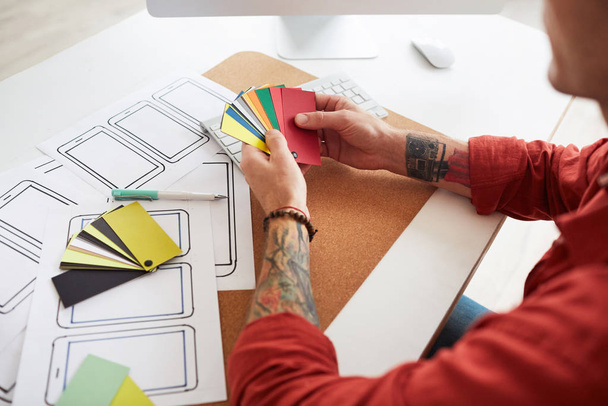 Magas szög közeli tetovált férfi kéz gazdaság színes mintákat, miközben kiválasztja paletta web design projekt, másolás helyet - Fotó, kép