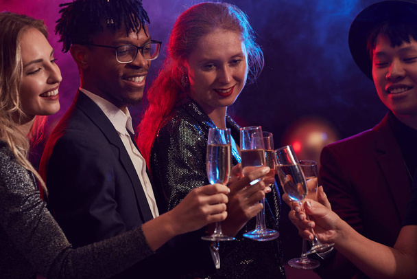 Cintura até retrato de jovens clinking taças de champanhe em smoky night club enquanto celebra feriados na festa, espaço de cópia
 - Foto, Imagem