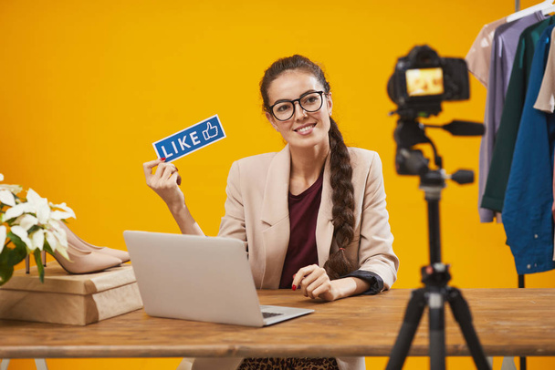 Porträt einer zeitgenössischen jungen Frau mit Likes und abonnieren Sie Wort und lächelt in die Kamera während der Dreharbeiten Video für Schönheit und Lifestyle-Kanal, Kopierraum - Foto, Bild