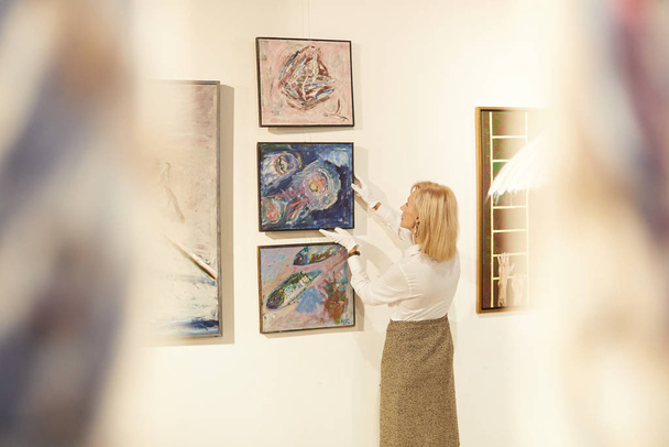 Back view portrait of female art expert hanging paintings while working in art gallery or museum, copy space - Foto, imagen