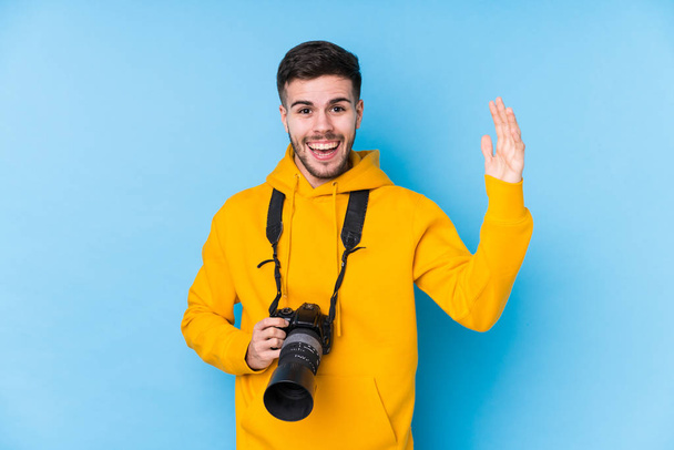 Jovem fotógrafo caucasiano isolado recebendo uma agradável surpresa, animado e levantando as mãos. - Foto, Imagem