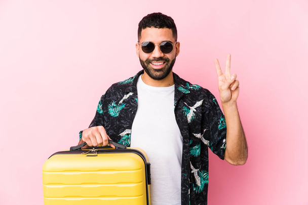 Молодий латинський чоловік тримає валізу, показуючи номер два пальцями
. - Фото, зображення