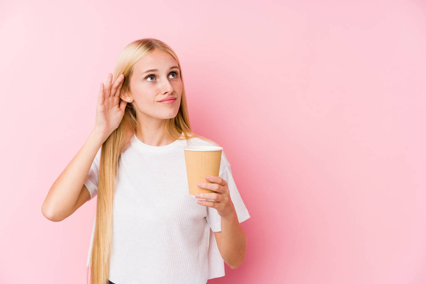 Joven chica rubia sosteniendo un café para llevar tratando de escuchar un chisme
. - Foto, Imagen