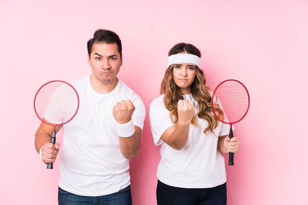 Young couple playing badminton isolated showing fist to camera, aggressive facial expression. - Fotoğraf, Görsel