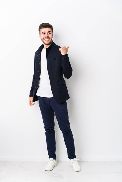Full body young caucasian man isolated points with thumb finger away, laughing and carefree. - Photo, Image