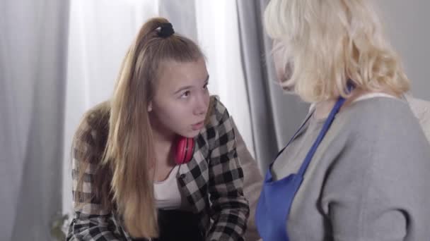 Close-up of cute Caucasian girl talking to blond mature woman. Grandmother hugging granddaughter and looking away. Support, care, family relationship. - Materiaali, video
